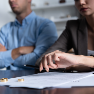 Man and woman sitting in front of divorce papers with wedding rings sitting on top of divorce papers